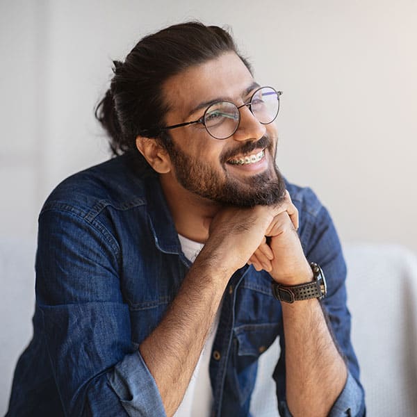 Smiling man with glasses and a beard, wearing a denim shirt, resting his chin on his hands.