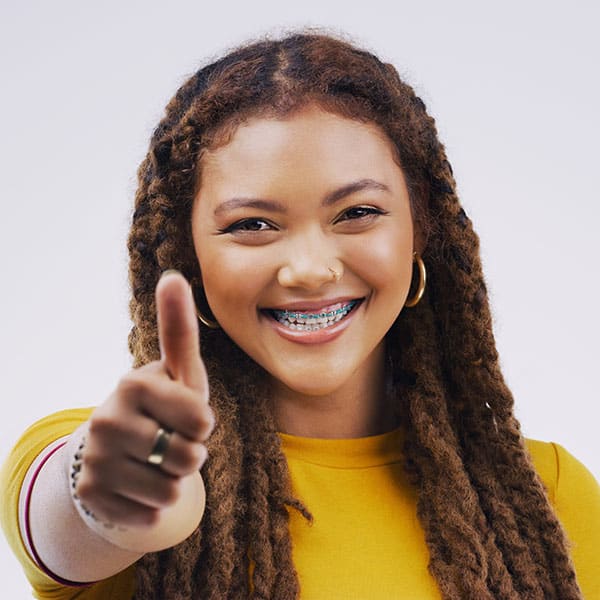 Smiling young woman with braces points at the viewer, wearing a yellow top.